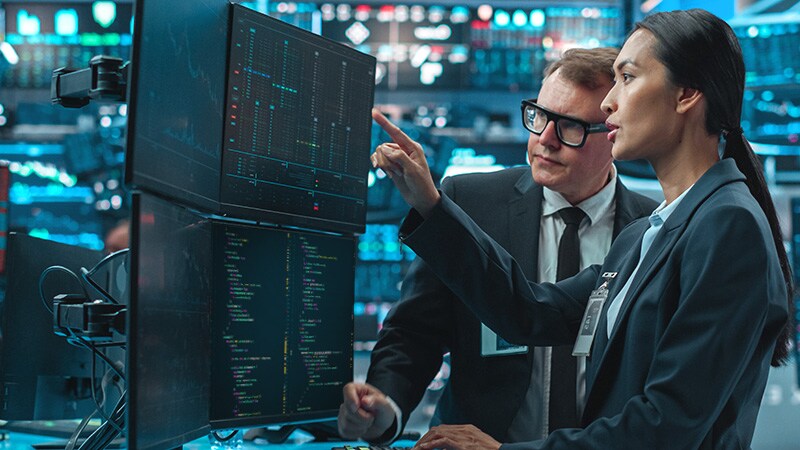 Two professionals in suits collaborating while examining a computer screen together.